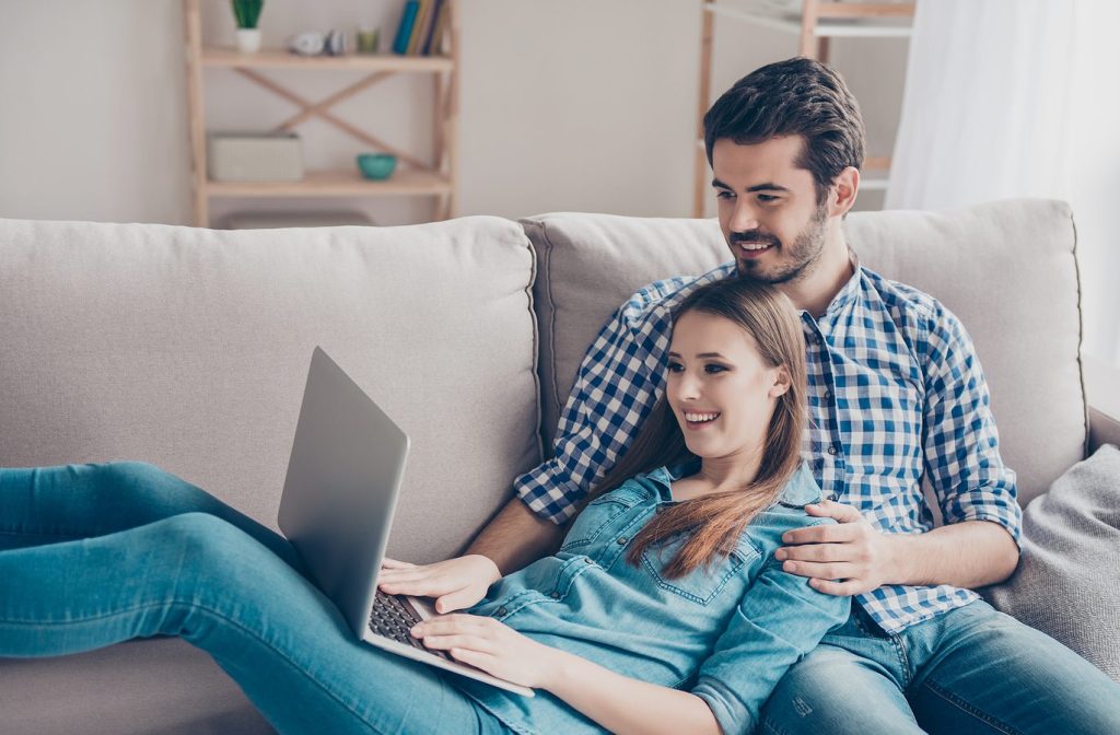 Young couple on couch with laptop, planning strategies to maximize savings and build financial growth.